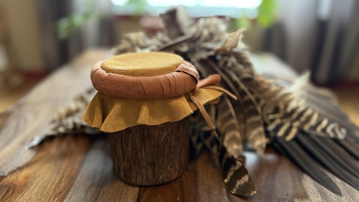 Un petit tambour en avant plan et une coiffe ornée de plumes rayés beiges et brunes.