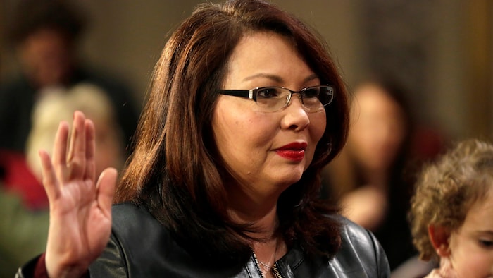 Tammy Duckworth, qui porte des lunettes, lève la main.