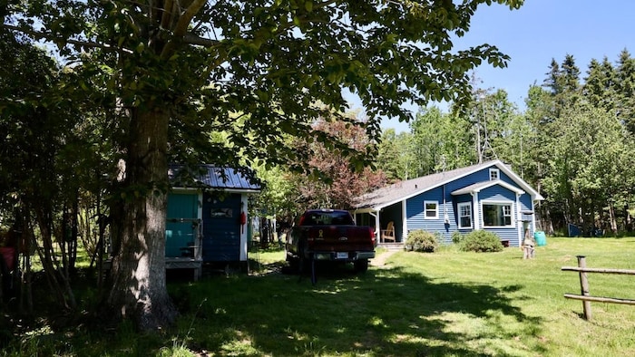 Deux bâtiments bleus et une camionnette sous des arbres dans un paysage estival.