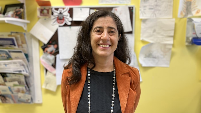 Tania Sarrouge debout dans une salle, souriante, se faire prendre en photo. 
