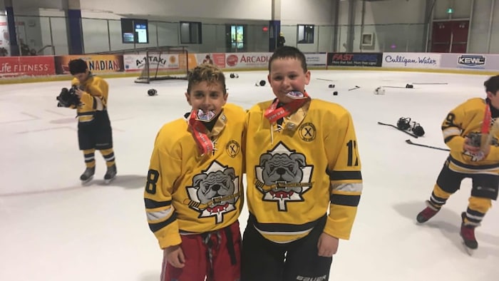 Tanner et un coéquipier posent pour une photo avec une médaille dans la bouche.