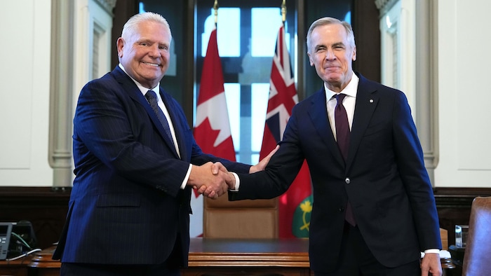 Doug Ford et Mark Carney se serrent la main devant un bureau, un drapeau canadien et un drapeau ontarien.