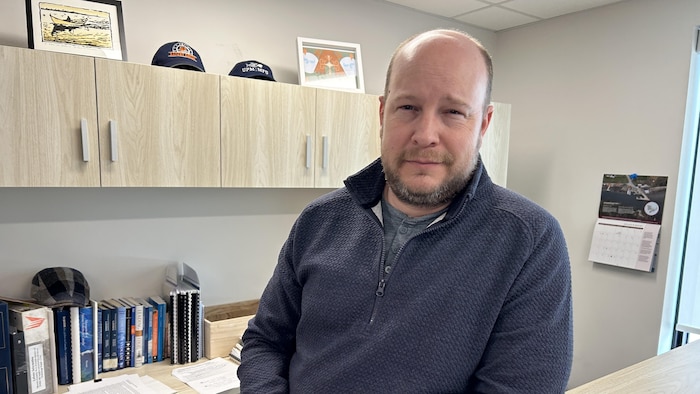 Martin Mallet est debout et accoté sur son bureau.