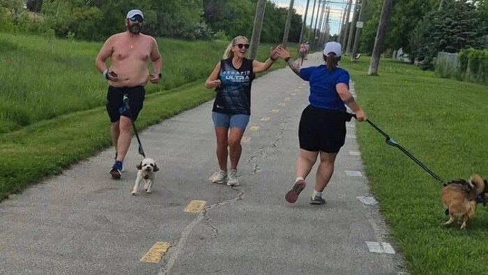 Deux coureuses se tapent dans la main. Un homme court torse nu en promenant son chien.