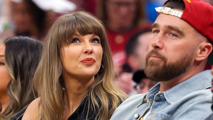 Taylor Swift et Travis Kelce entourés de personnes dans un aréna. 