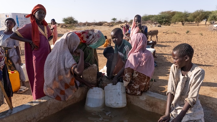 Des enfants et des femmes près d'un puits d'eau brunâtre.
