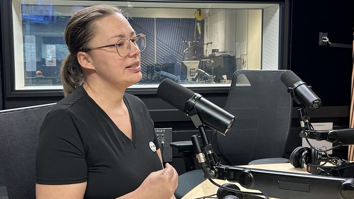 Une femme assise dans un studio de radio parle au micro. 