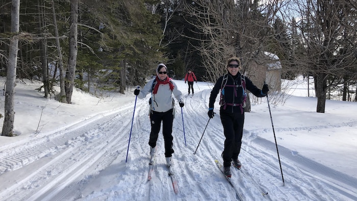 Deux femmes souriantes s'avancent au milieu d'une piste de ski de fond.