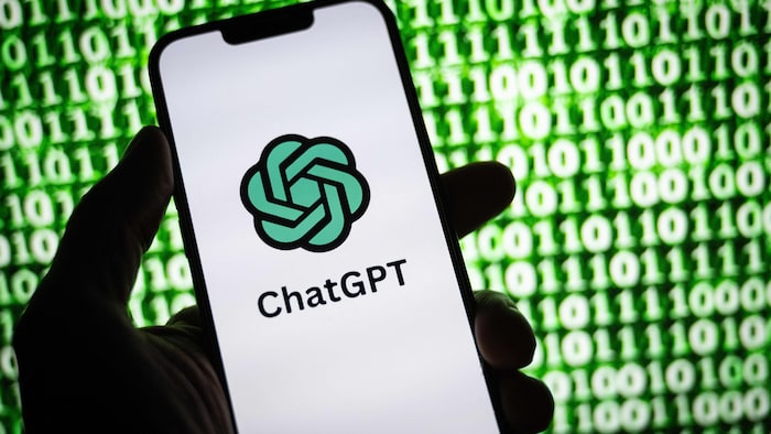 Une main tient un téléphone dont l'écran montre le logo de ChatGPT. 