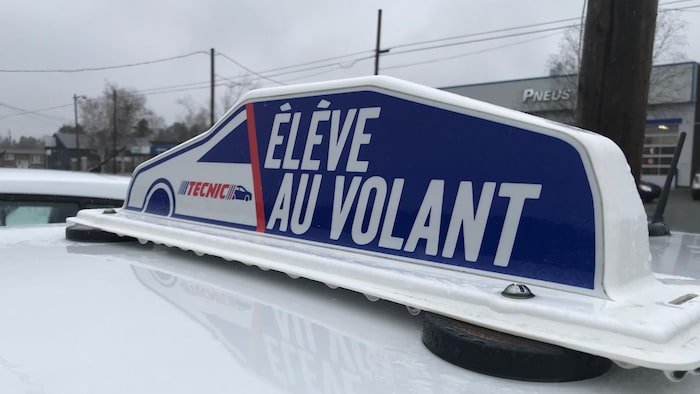 Une affiche sur le toit d'une voiture indique «Élève au volant».