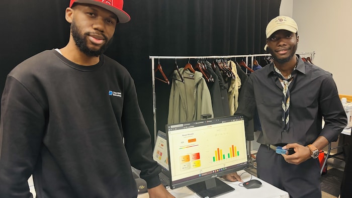 Deux jeunes posent devant une table où est installé un ordinateur présentant des graphiques à l'écran