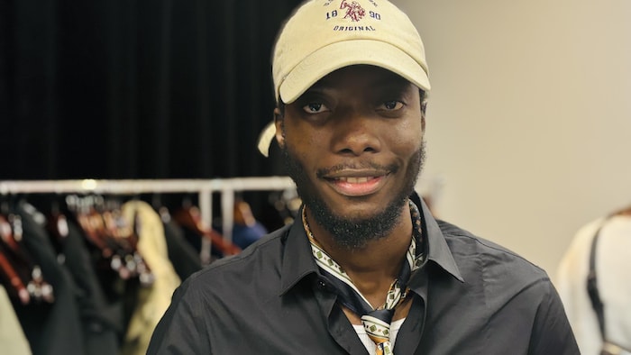Coiffé d'une casquette et portant une cravate, le jeune homme sourit