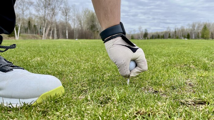 Un joueur de golf tient une balle sur un tee au Club de golf de Baie-Comeau.