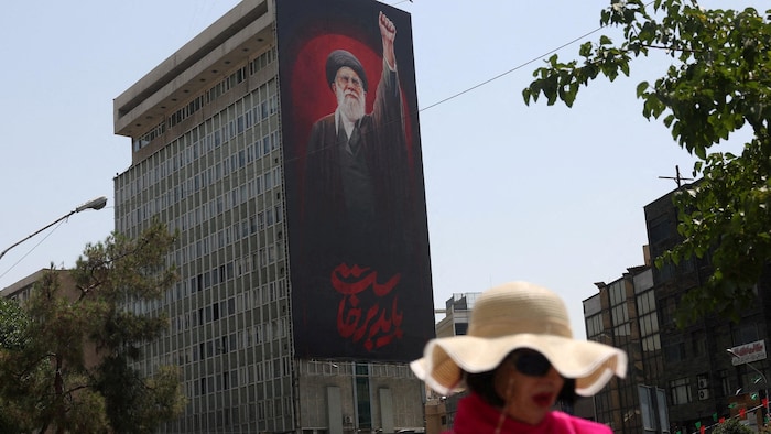Une femme portant un chapeau passe devant un panneau d'affichage représentant un homme vêtu de noir levant le poing.