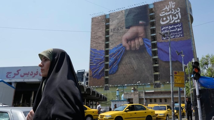 Une femme voilée passe devant une murale.