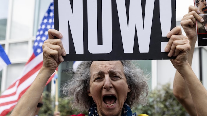 Une femme qui crie brandit une pancarte sur laquelle il est écrit « NOW » (maintenant).