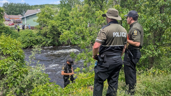 Trois policiers regardent vers un ruisseau.