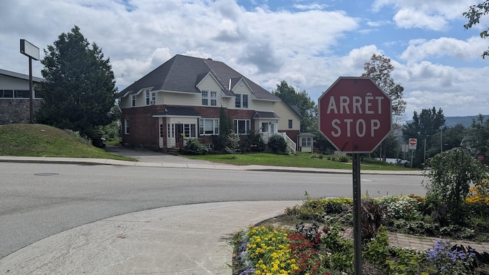 Coin de rue avec panneau arrêt-stop et jardin de fleurs. Derrière, une maison typique de Témiscaming.