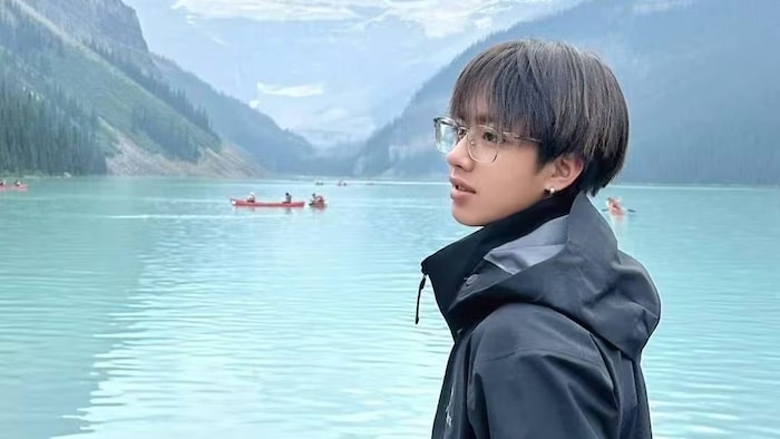 Une personne se tient devant un lac, entouré de montagnes.