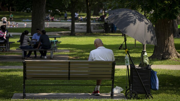 Un Torontois est assis sur un banc et se protège du soleil avec un parasol. 