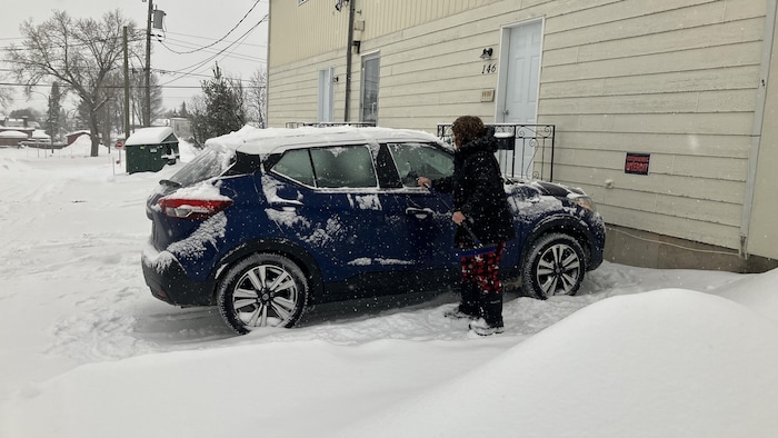 Une femme déneige son véhicule et déglace la vitre côté passager.