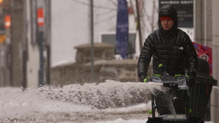 Un homme souffle de la neige qui recouvre un trottoir de Québec.