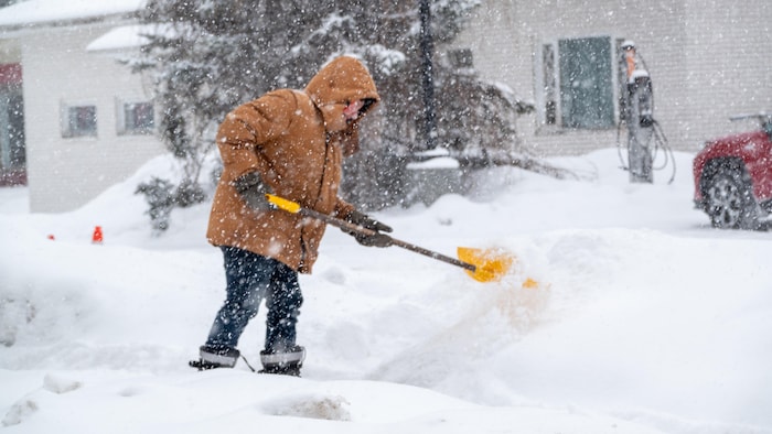 Un citoyen qui déneige l'entrée d'un commerce.