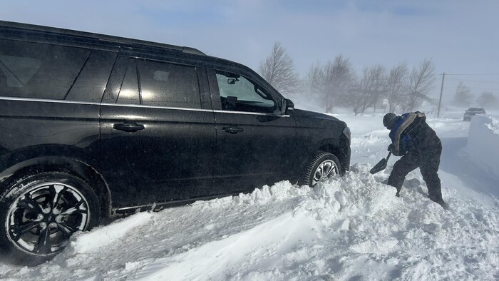 Un homme pellette la neige à l'avant d'un véhicule pour le dégager.