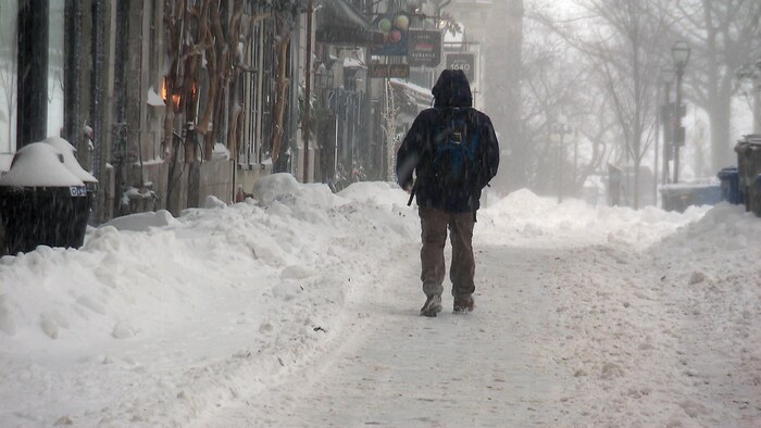 Un marcheur dans une rue enneigée.