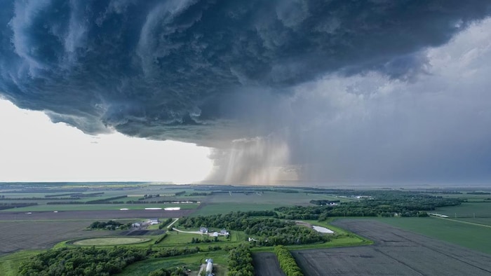 Un énorme nuage sombre domine les fermes sur une photo prise du ciel. La pluie tombe au loin sur le côté droit du nuage.