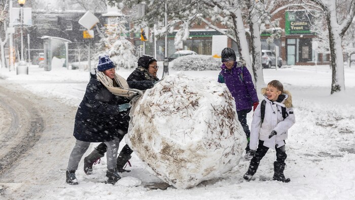 Des enfants poussent une énorme balle de neige.