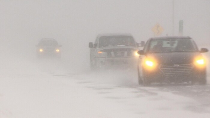 Des bourrasques soufflent de la neige devant les voitures.