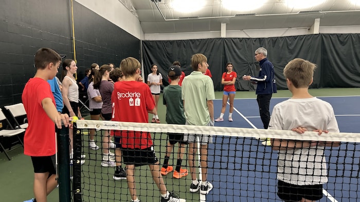 Des jeunes qui écoutent un entraîneur sur un terrain de tennis.