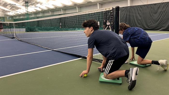 Deux joueurs agenouillés près d'un filet de tennis.