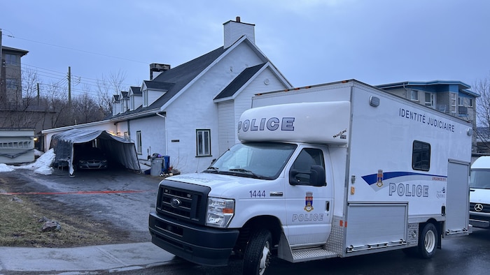 Un véhicule de la police de Québec est garé devant une maison entourée de ruban.