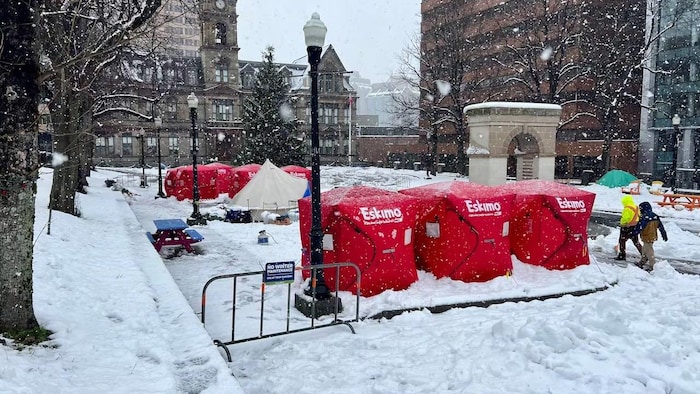 Sept grosses tentes carrées rouges pour la pêche sur glace sont posées sur une place publique, pendant qu'il neige.