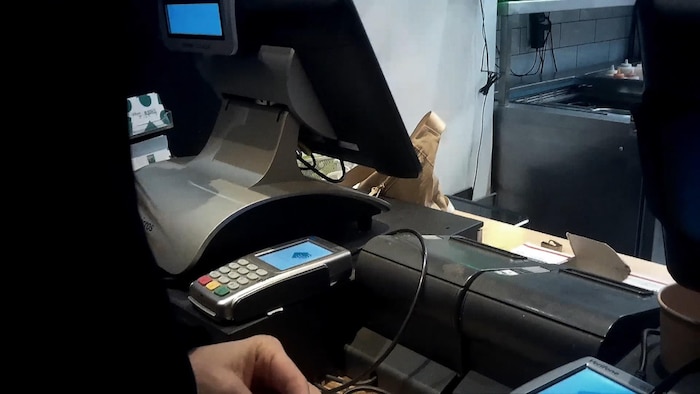 Un terminal de paiement est situé à côté de la caisse enregistreuse d'un comptoir de restauration rapide.