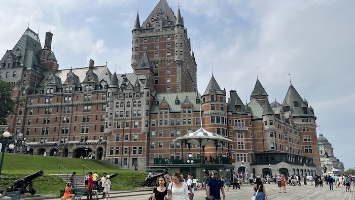 Des touristes déambulent sur une large terrasse de bois devant un immense hôtel aux allures de château.