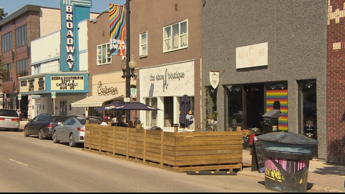 Avenue Broadway à Saskatoon : une terrasse clôturée et disposant de tonnelles est posée sur un emplacement qui été réservé au stationnement de voitures en face d'un commerce.