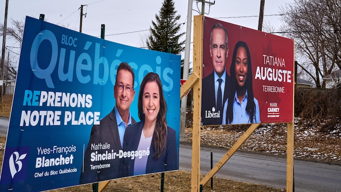 Une affiche du Bloc québécois à côté d'une affiche du Parti libéral du Canada montrent les chefs et leurs candidates respectives.