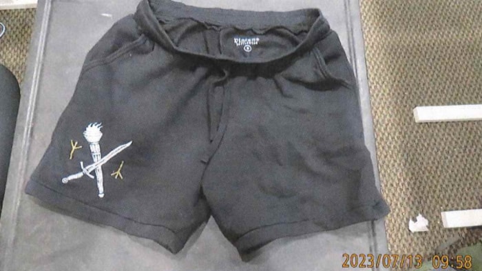 Un short de gymnastique gris avec sur la cuisse droite un dessin blanc représentant une épée formant une croix avec un flambeau.