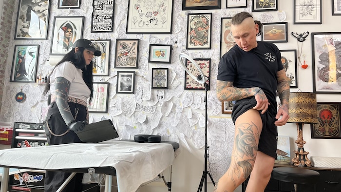 Un homme montre les tatouages sur sa jambe à une femme.
