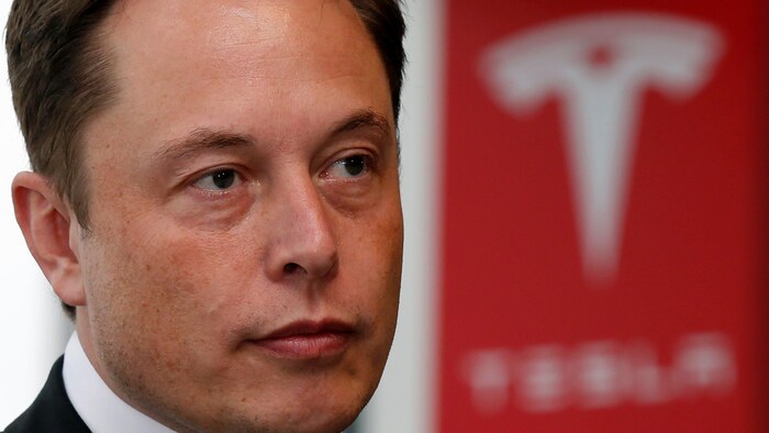 Elon Musk devant un logo de Tesla.