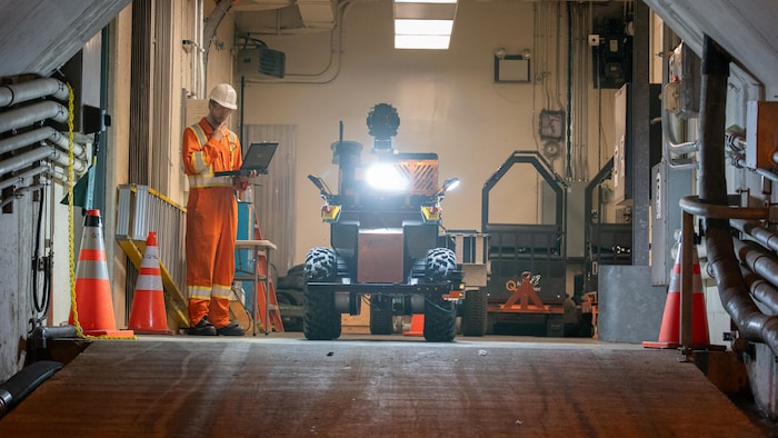 Un homme regarde son ordinateur près d'un robot dans un tunnel.