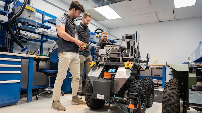 Trois hommes regardent un robot sur roue dans un atelier.