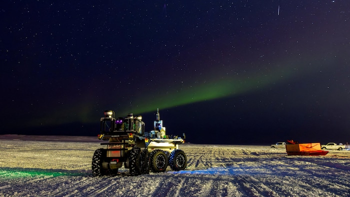 Un robot sur la neige la nuit lors d'une aurore boréale.