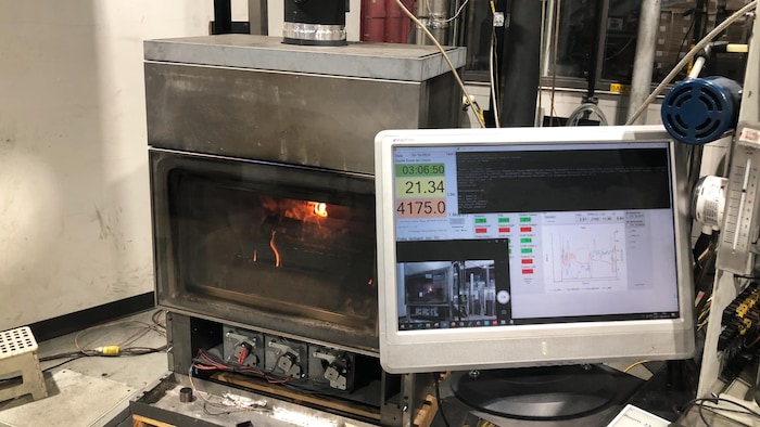 Un appareil de chauffage au bois soumis à un test en laboratoire. À l’avant-plan, un moniteur affiche différentes données.