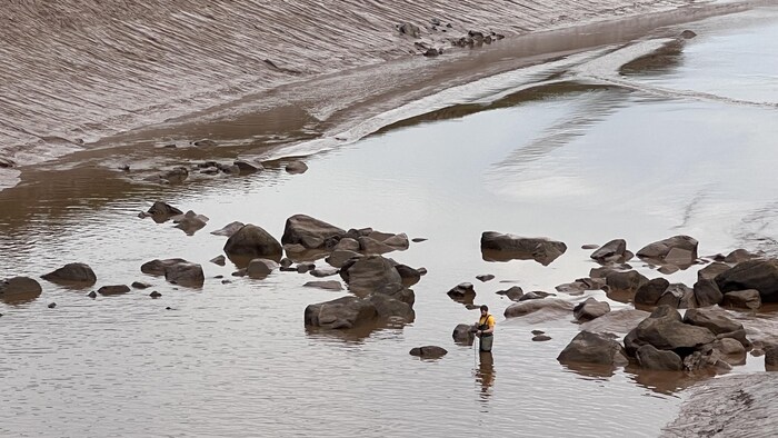 Un homme avec un appareil, dans l'eau jusqu'à la taille.
