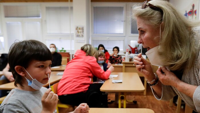 Une femme et un jeune enfant dans une classe utilise un écouvillon pour prendre un échantillon dans leurs narines.