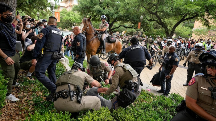 Des agents procèdent à une arrestation pendant la manifestation, sous le regard d'un policier à cheval. 